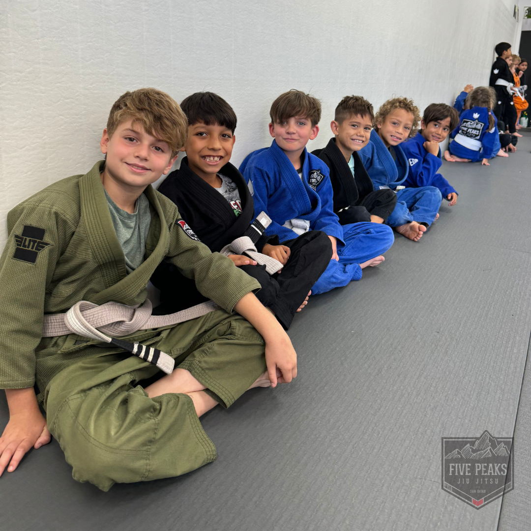 Group of kids sitting together smiling after jiu jitsu class at Five Peaks Jiu Jitsu