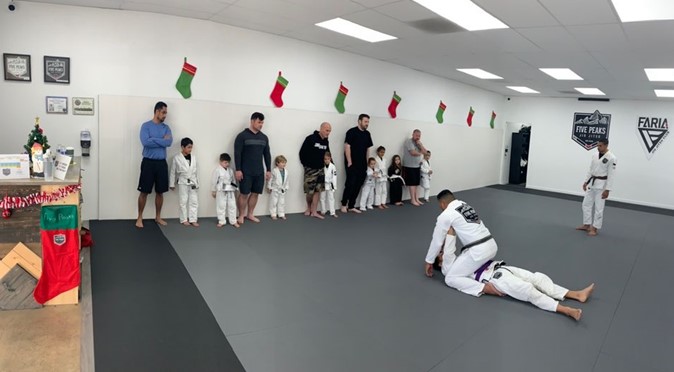 Instructor demonstrating technique while students and parents watch on the mat at Five Peaks Jiu Jitsu