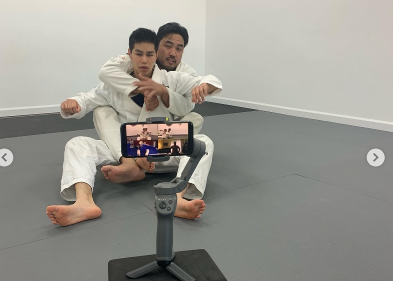 Coaches conducting virtual jiu jitsu technique instruction with online student stream