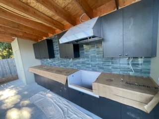 Outdoor kitchen custom cabinetry, tile backsplash, and range hood under covered patio