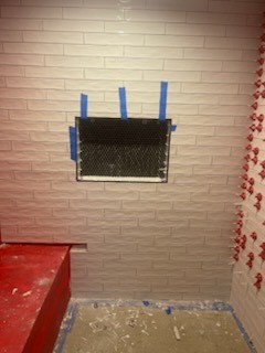 White brick-pattern tile wall installation with taped-off niche cutout in progress
