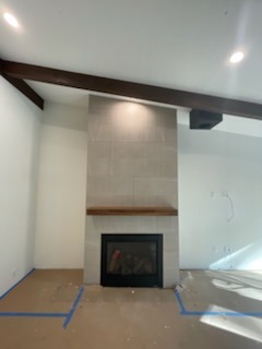 Contemporary tile fireplace surround installation with custom wood mantle beam