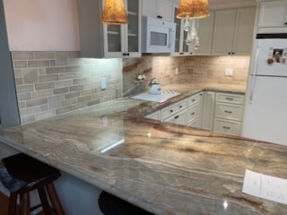 Kitchen remodel featuring polished natural stone countertop, tile backsplash, and pendant lighting