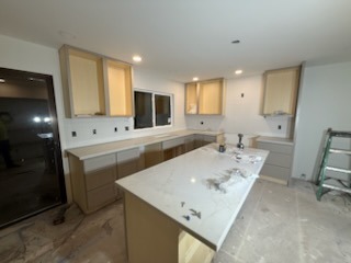Custom kitchen island with marble-look quartz countertops and natural wood cabinetry under construction