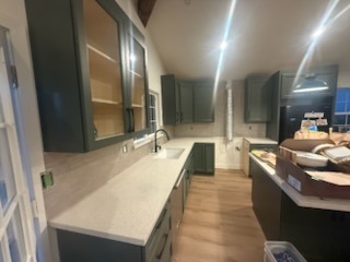 Sage green kitchen cabinetry with quartz countertops and wood-look flooring installation