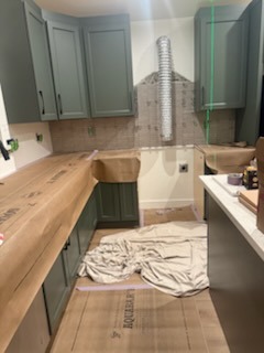 Custom wood countertop installation on green cabinetry with range hood and tile backsplash prep