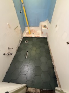 Finished dark green hexagonal floor tile installation with crisp grout lines in a remodeled bathroom suite