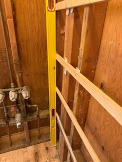 Precision wall framing and stud leveling with a 4-foot spirit level for custom bathroom plumbing and shower install