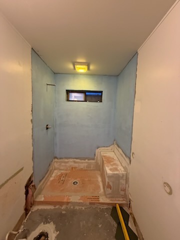 Walk-in shower enclosure with built-in bench seating, custom window cut-out, waterproof membrane and sloped mortar bed
