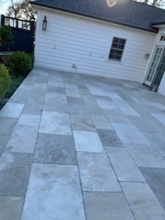 Large outdoor paver patio installation with stone pattern design next to home exterior