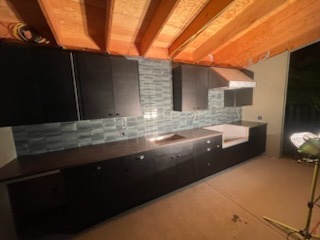 Dark modern kitchen cabinetry with mosaic tile backsplash and exposed wood beam ceiling