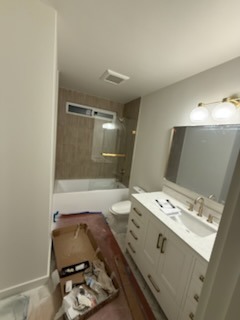 Bathroom remodel with tiled tub surround, glass shower door, and dual-sink vanity with gold fixtures