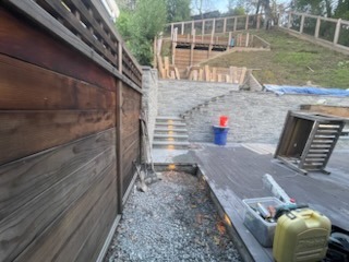 Stack stone retaining wall, outdoor patio stairs with integrated step lighting, and custom fencing