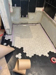 Hexagon mosaic tile shower floor installation in progress with cement board walls