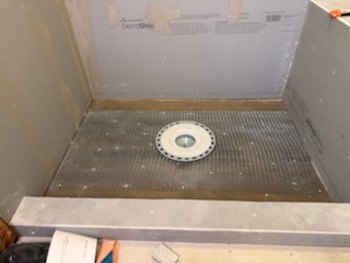 Custom shower pan preparation with centered drain assembly, metal lath reinforcement, and cement backer board curbs