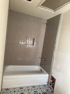 Alcove bathtub installation with vertical subway tile surround and decorative patterned floor tile