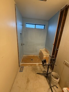 Shower prep with waterproofing membrane, bench framing, and high transom window