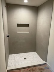 Modern walk-in shower featuring large format grey wall tile, mosaic tile floor, and built-in niche