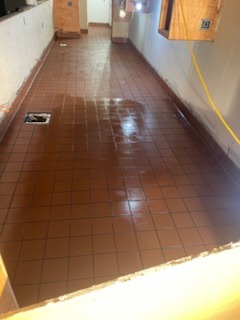 Brown ceramic tile flooring installation in a narrow hallway with floor drain