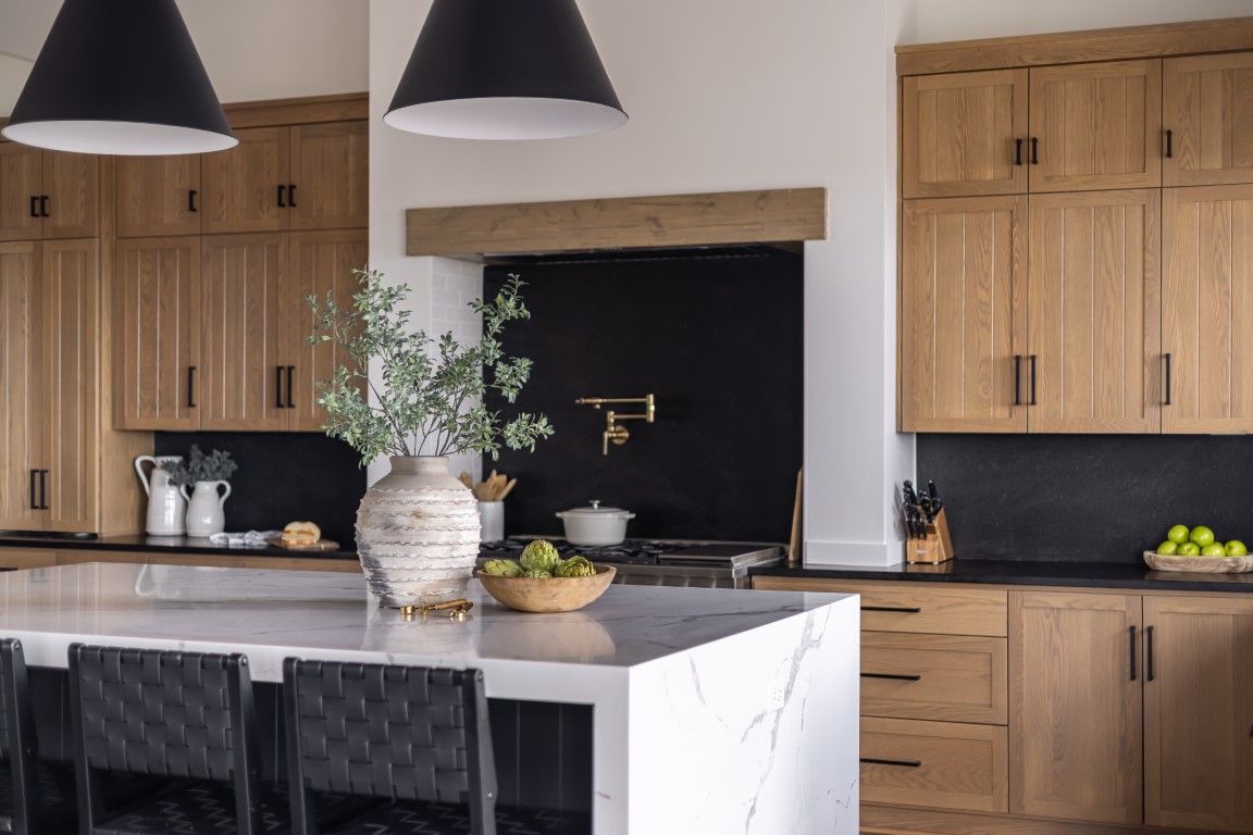 Luxury kitchen remodeling in Surprise AZ featuring custom natural oak cabinets, quartz waterfall island, black accent range wall and brass fixtures