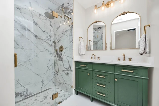 Master bathroom remodel in Surprise AZ featuring custom green vanity, gold hardware, dual arched mirrors and marble tile walk-in shower