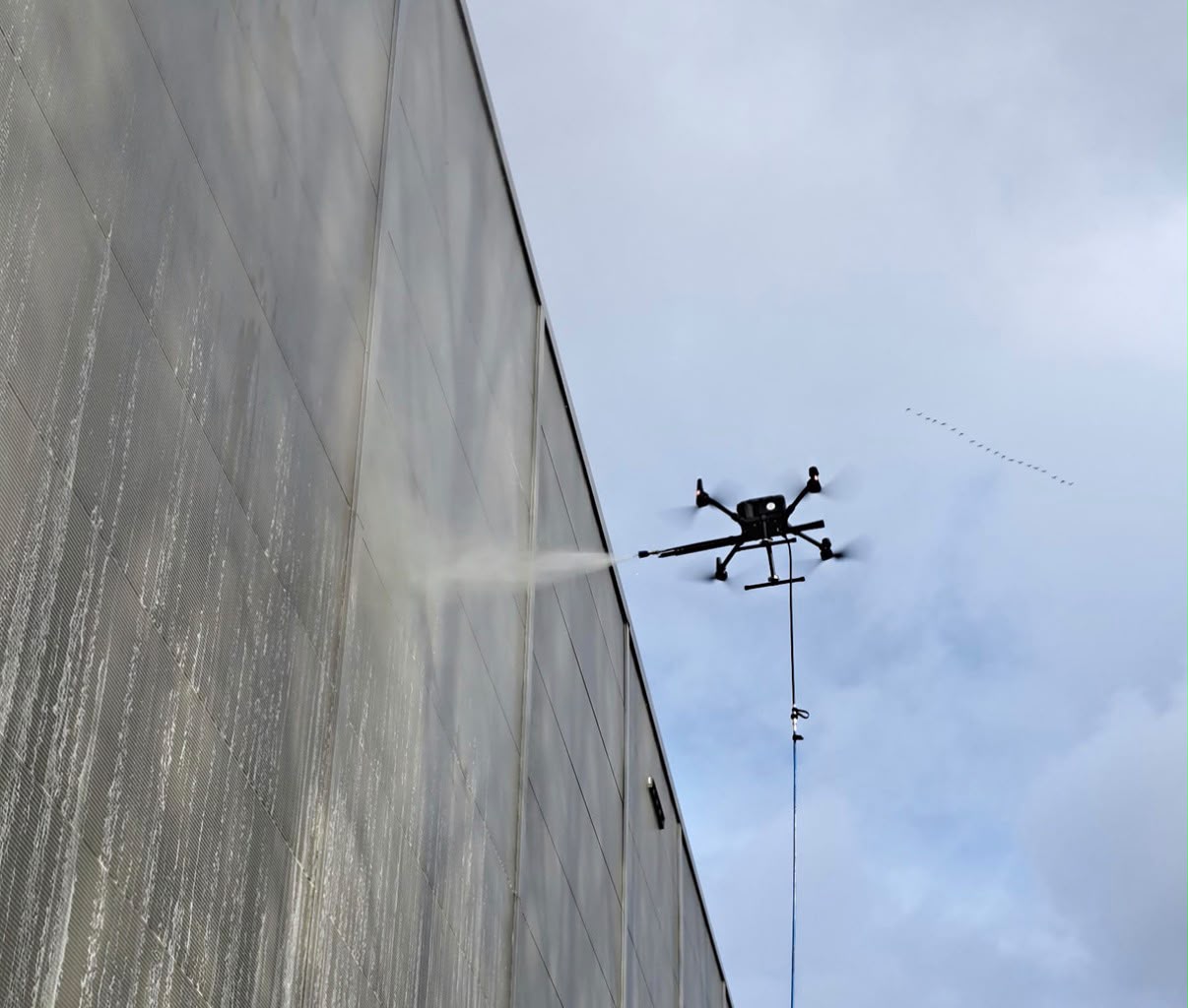 Chronos-reinigingsdrone spuit onder hoge druk een hoge gevel van een industrieel gebouw schoon