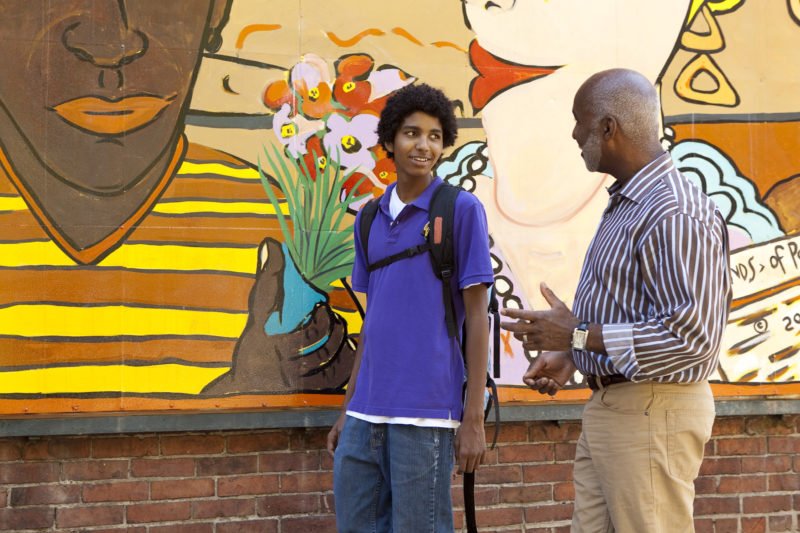 An adult and teenager talking in front of a colorful mural.