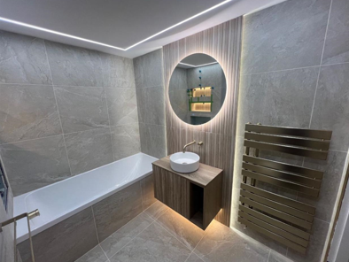 Modern bathroom with round mirror, timber vanity unit and bronze towel radiator