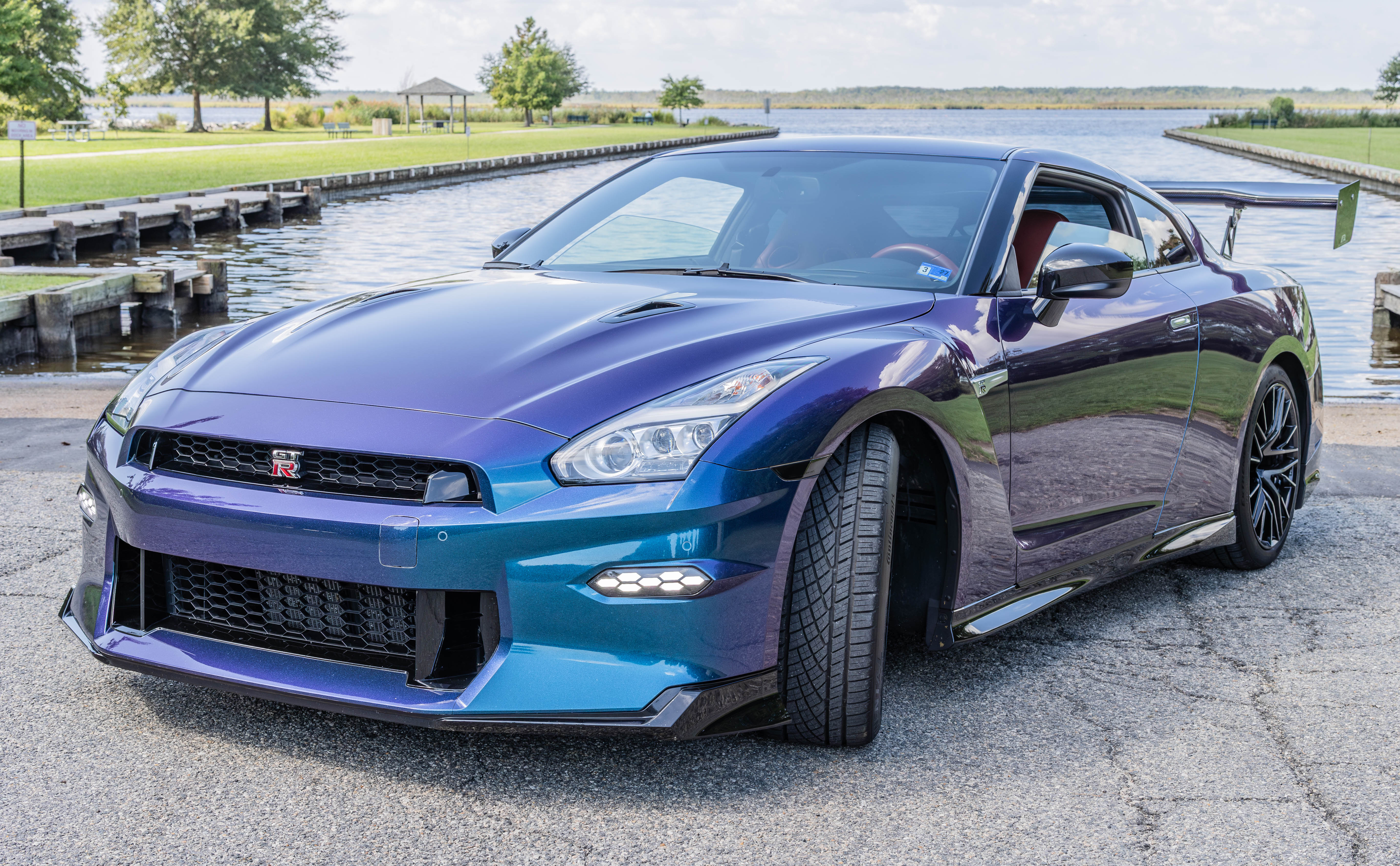 2024 Nissan GT-R Premium front end with Amber Red interior visible through the windshield, parked at a lakeside dock