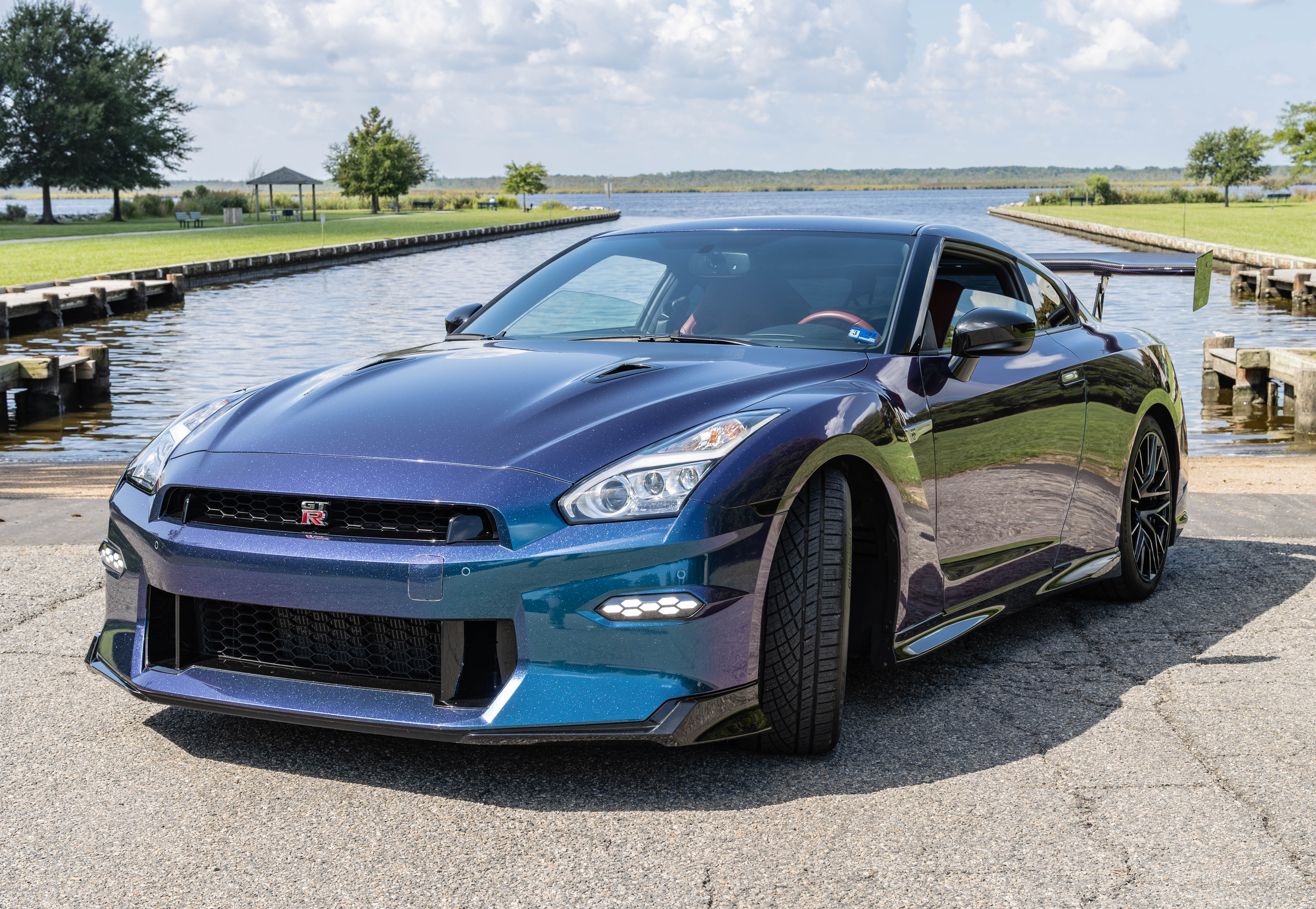 2024 Nissan GT-R Premium three-quarter view at the dock showing the rear wing and Amber Red cockpit
