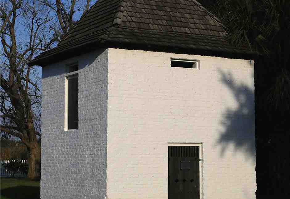 White brick historic outbuilding with dark shingle roof on plantation grounds