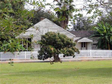 Rustic weathered wooden plantation house behind a white picket fence