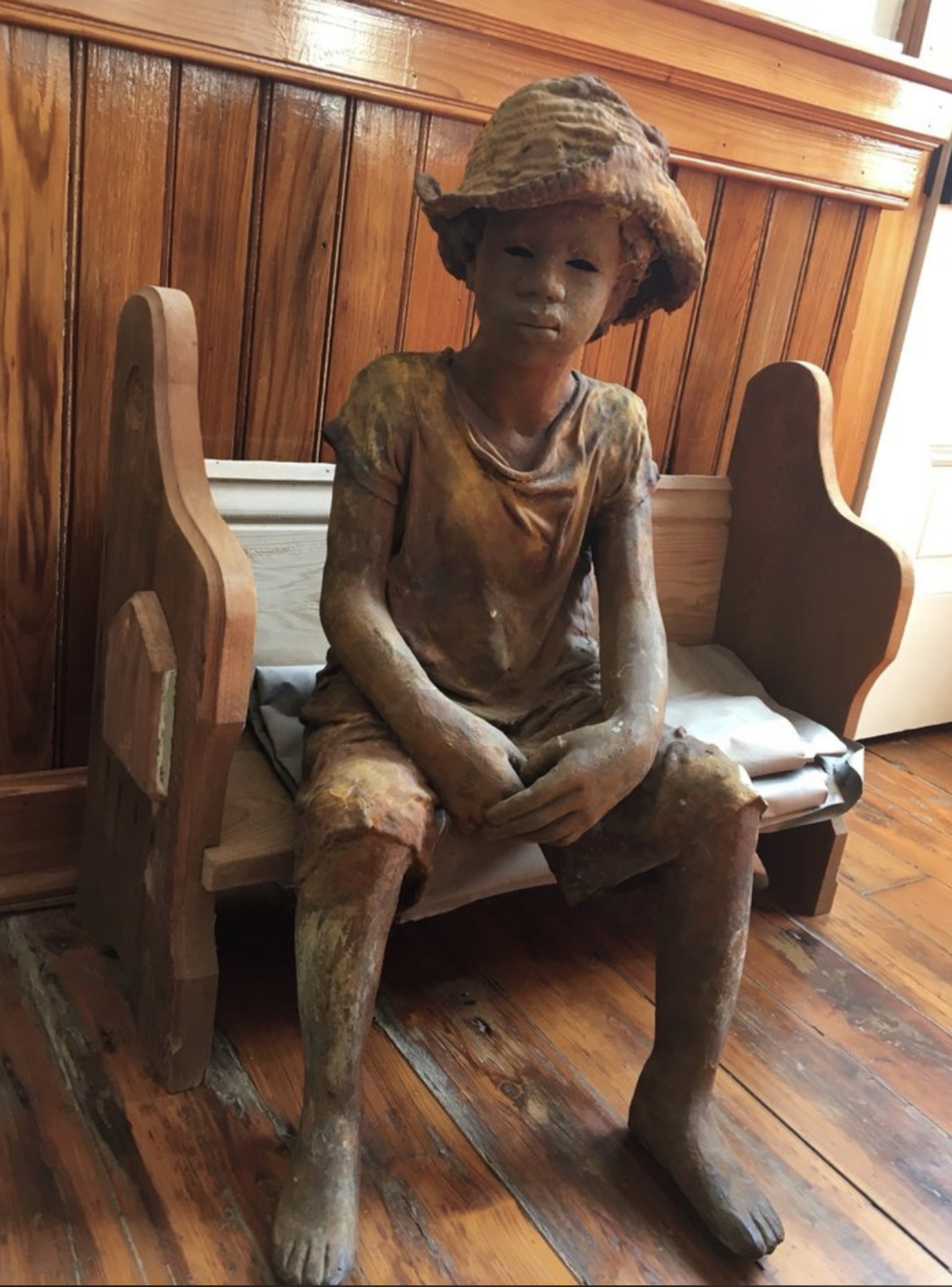 Sculpted child statue seated on wooden bench in hat inside plantation building