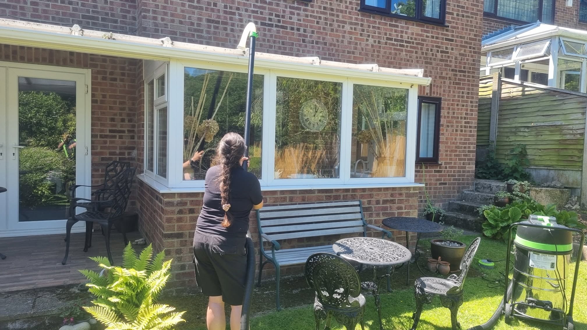 Julie on a roof clearing thick moss from a gutter by hand during a vacuuming job