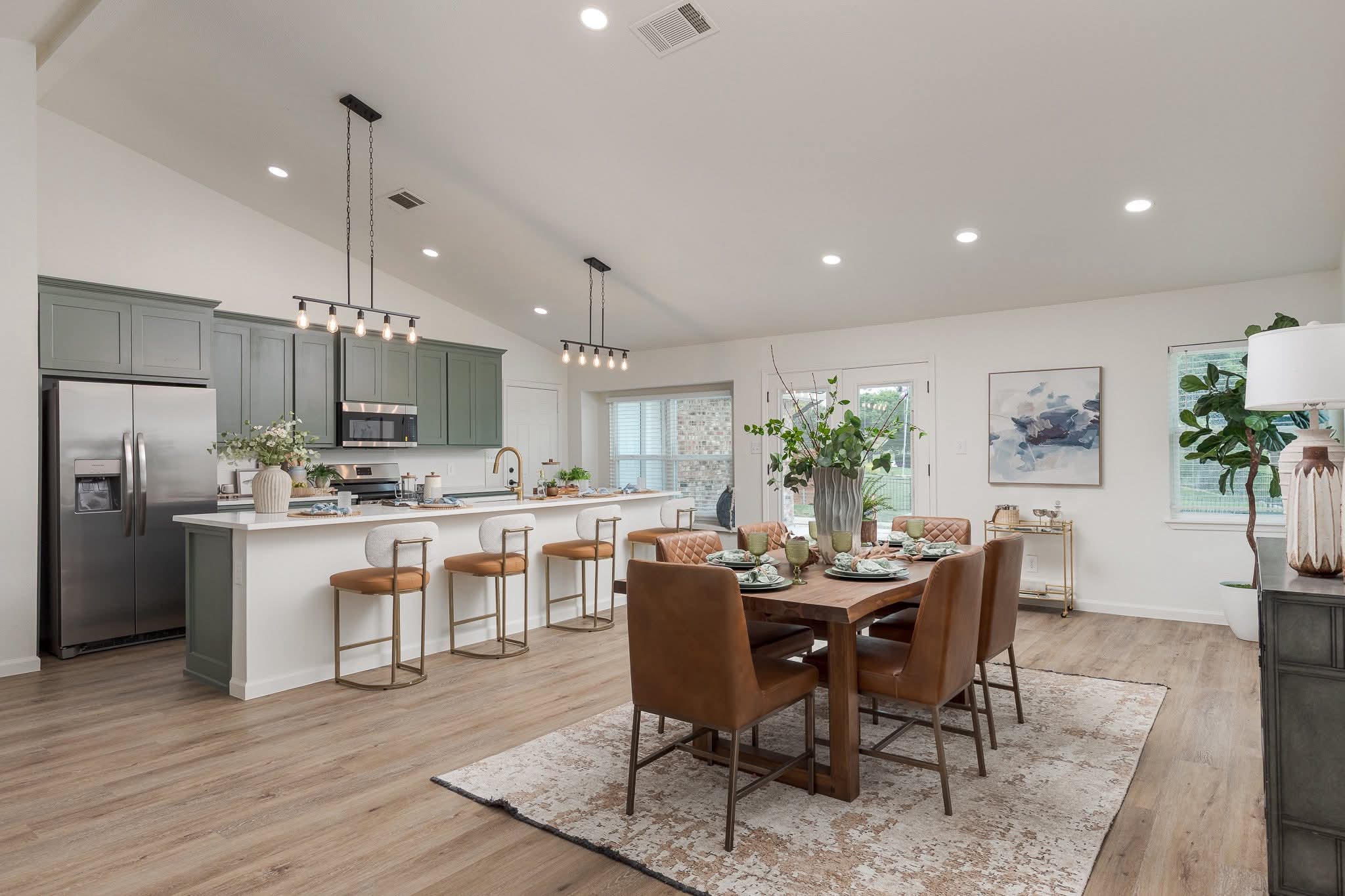 Elegantly staged open kitchen and dining area with sage cabinets and leather seating
