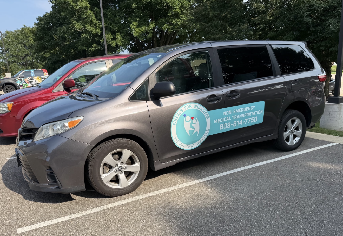 Wheels for Wellness wheelchair-accessible van in Madison, WI — grey charcoal van with aqua badge and a ramp for wheelchair access