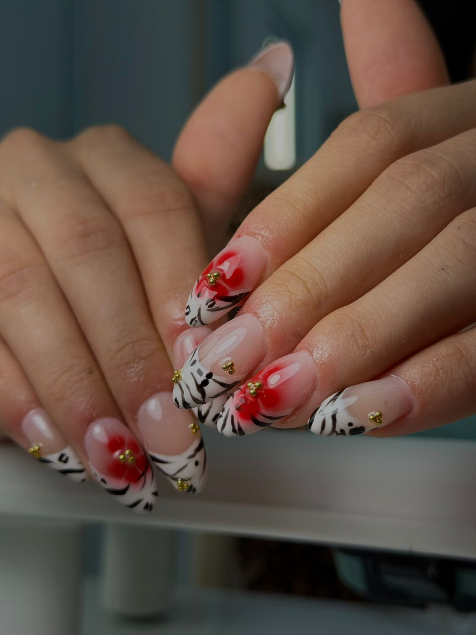 Diseño de uñas profesional con detalles florales rojos y dorados