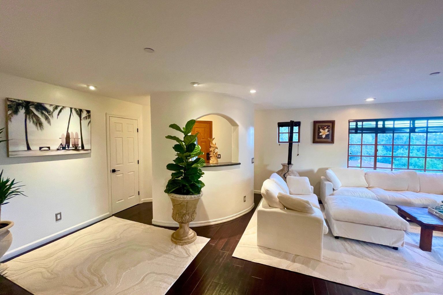 Living room with curved architectural wall, white upholstered sofas, hardwood floors, and a large window framing hillside views