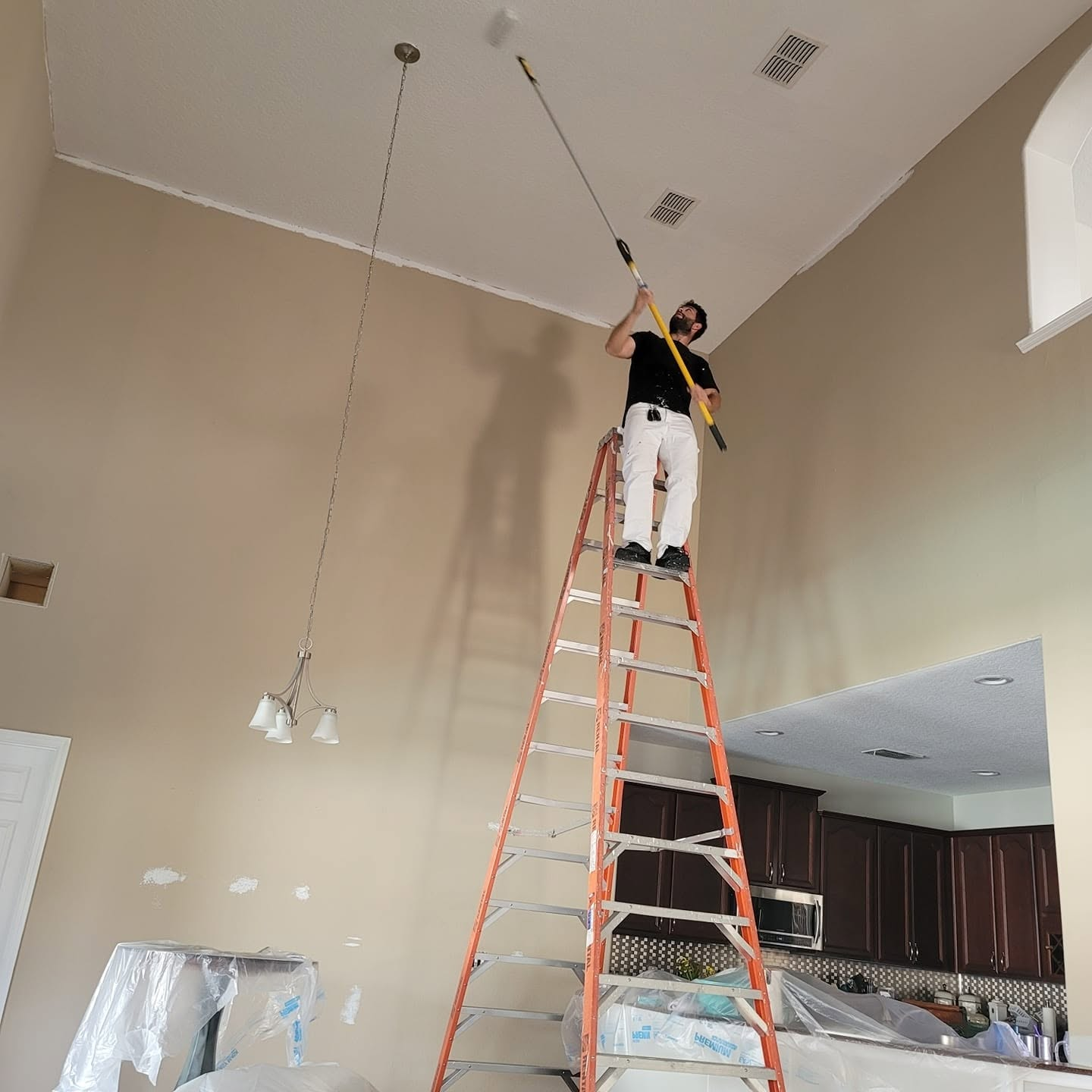 Fine Line painter cutting high interior walls from an extension ladder