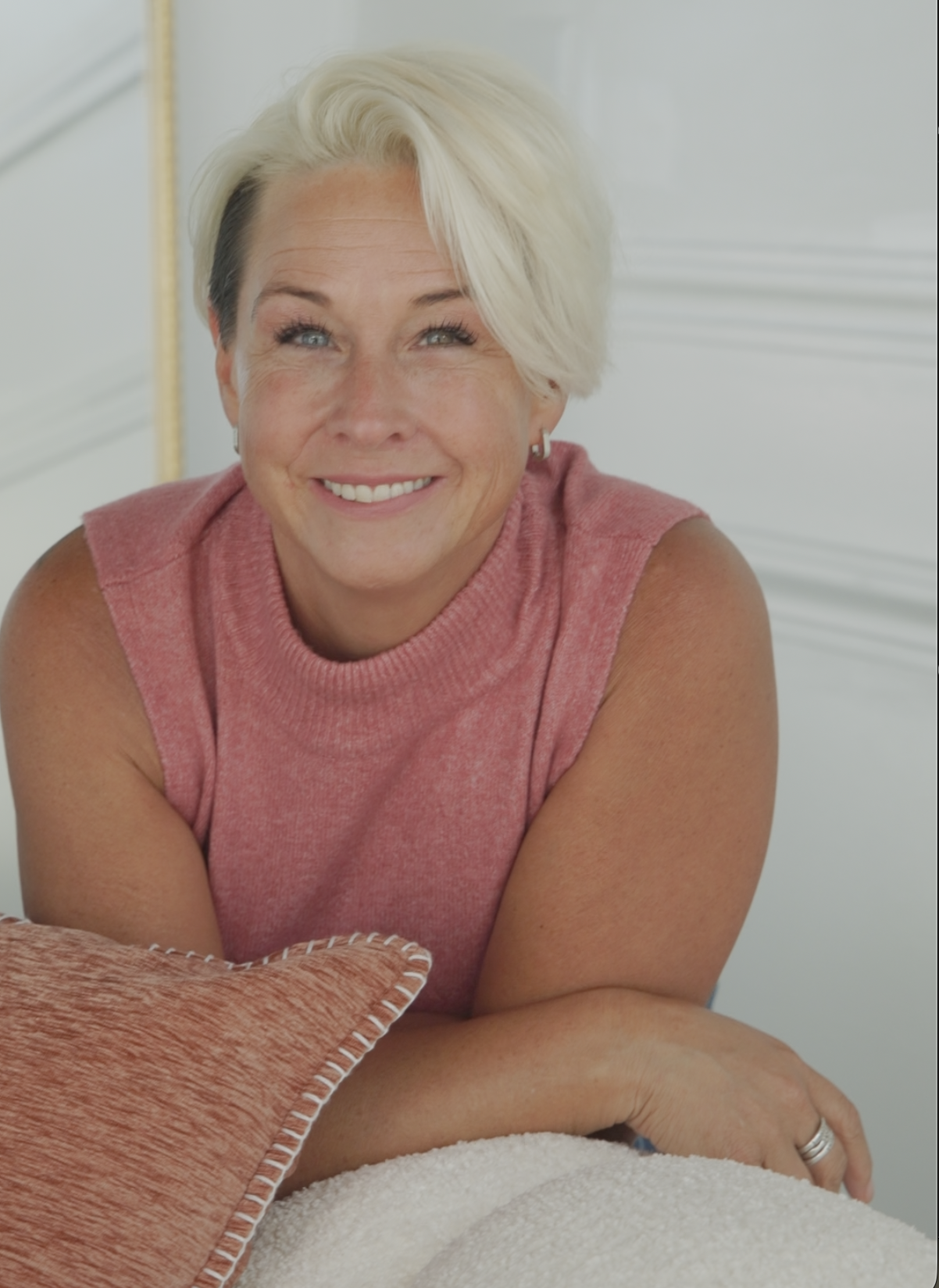 Lori smiling warmly in a heathered blush pink sleeveless knit top