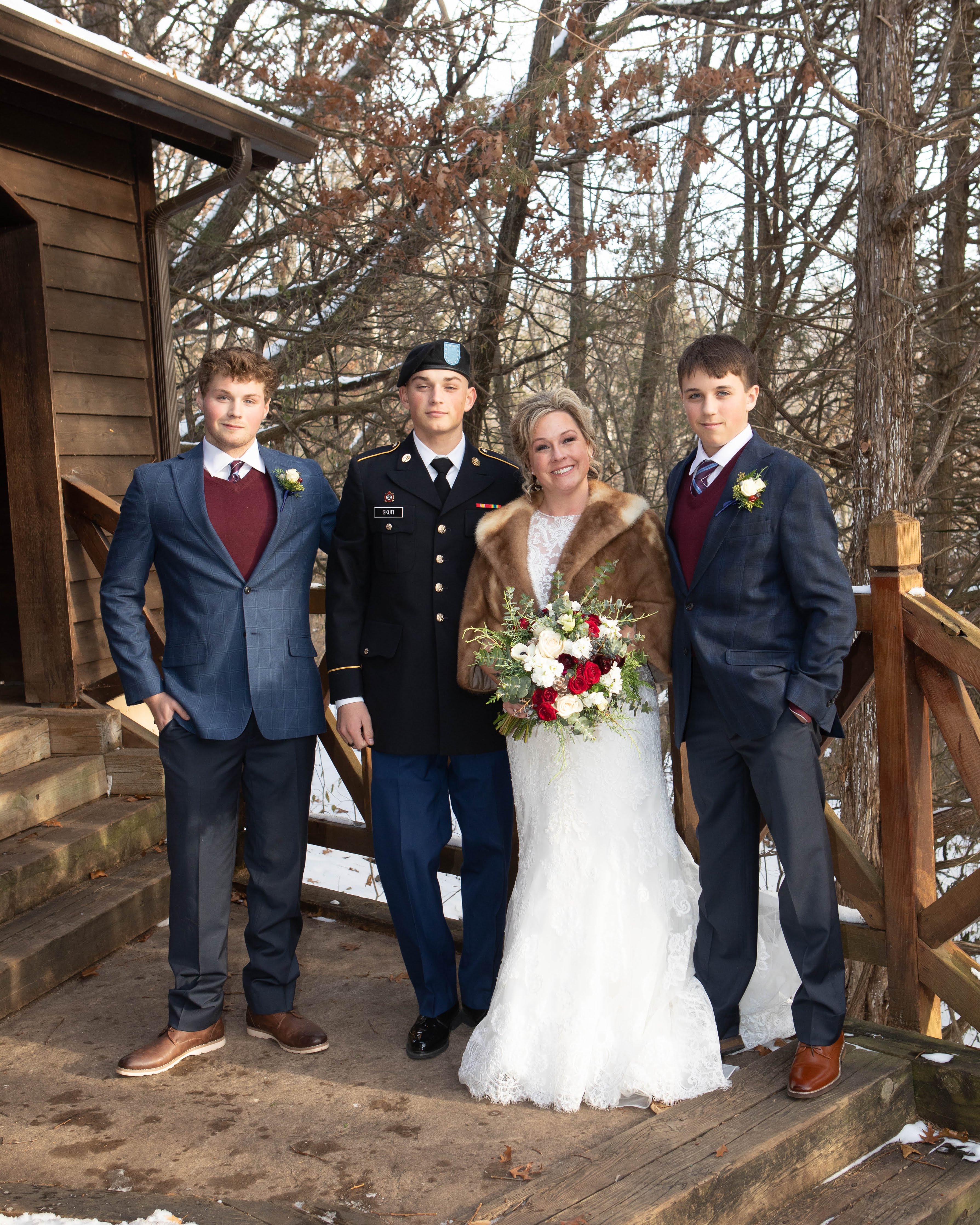 Lori on her wedding day in a lace gown and fur wrap standing with her three sons