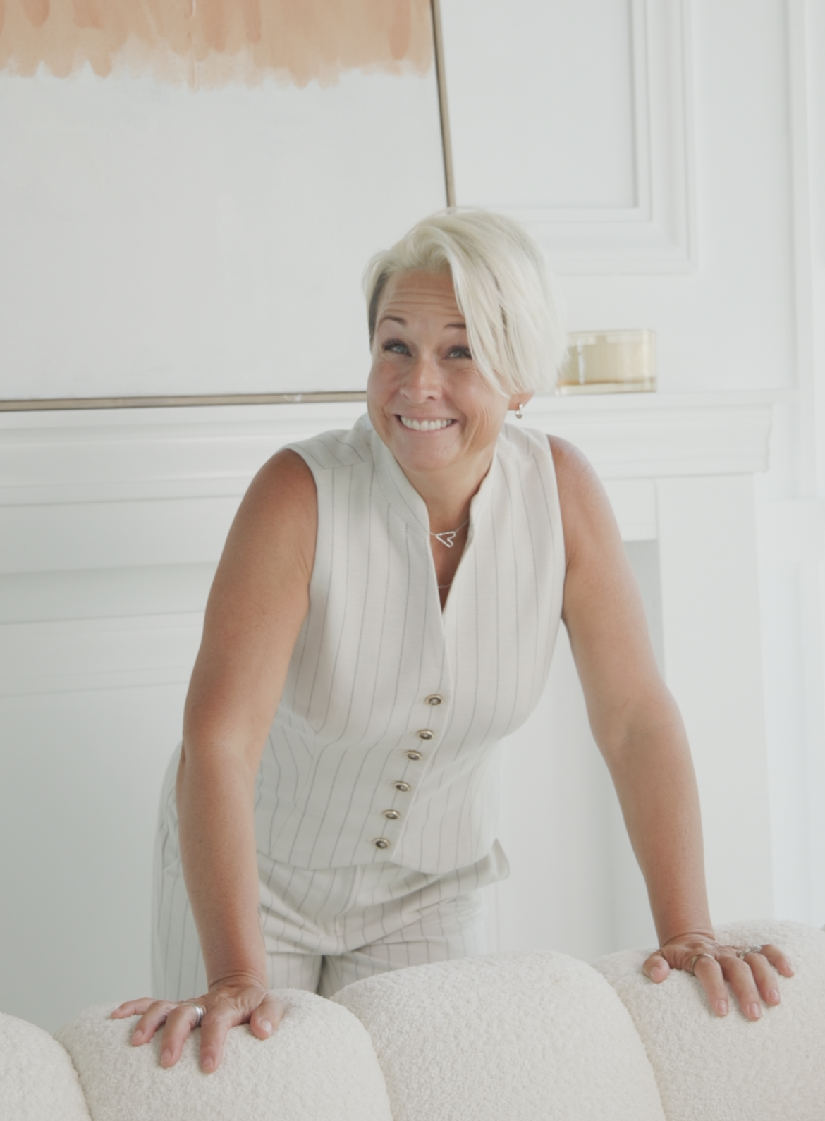 Lori Christophersen in a cream pinstripe outfit smiling and leaning over the back of a cream couch