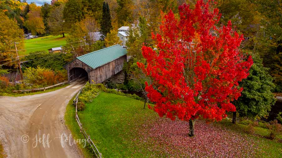 Bright New England autumn foliage over a Vermont covered bridge in vibrant red, orange, and gold