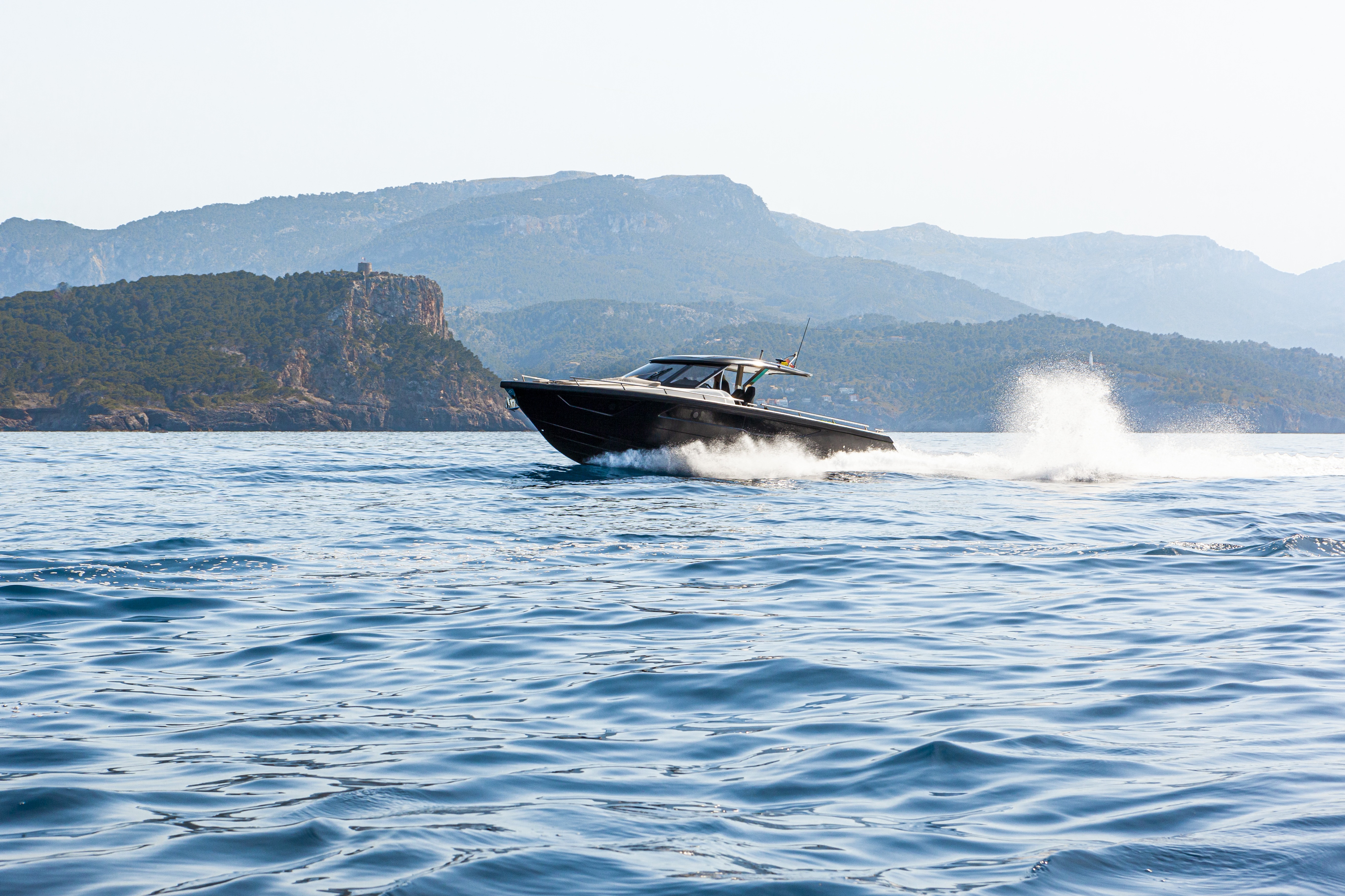 Sleek luxury yacht speeding past dramatic coastal cliffs in Italy