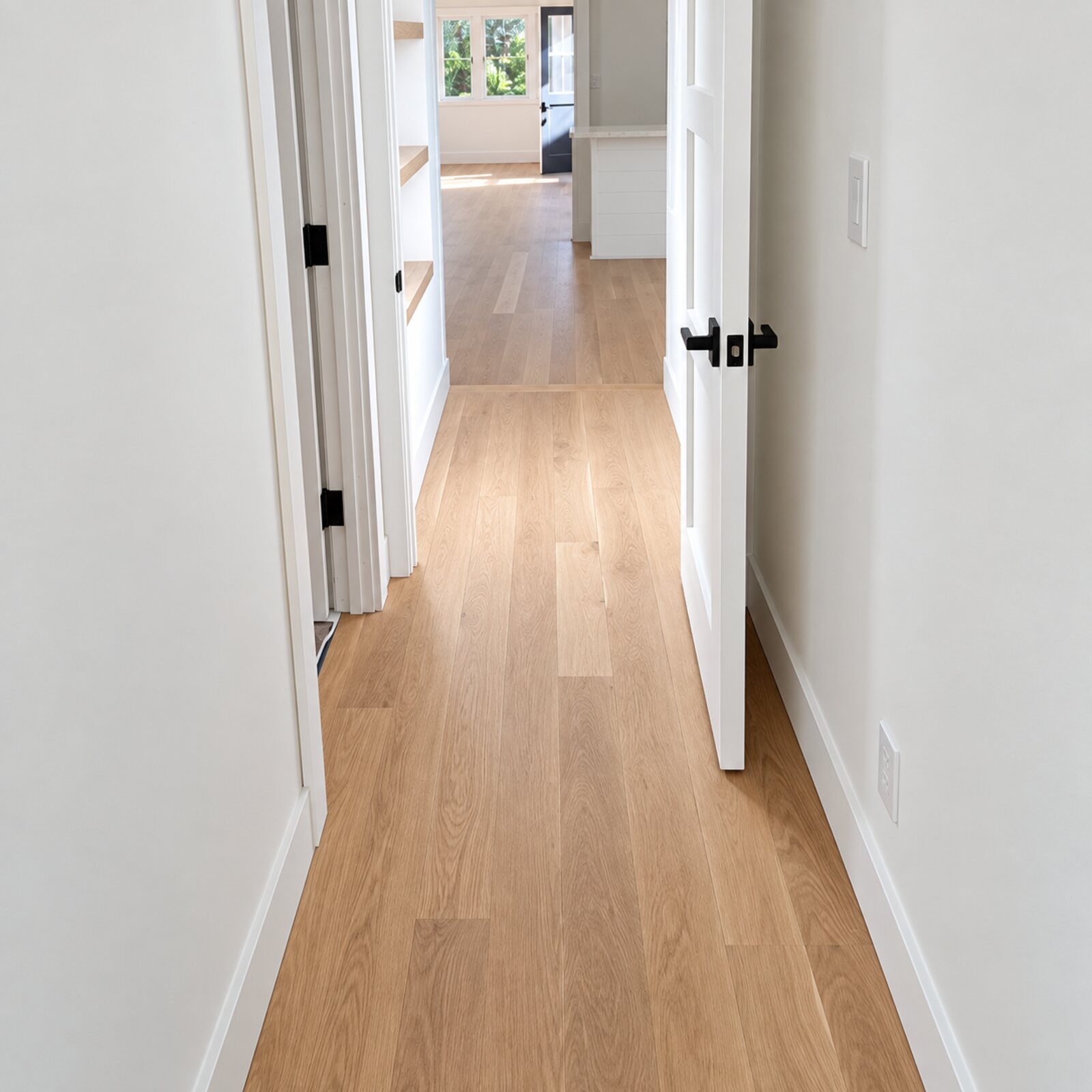 Light oak flooring running down a hallway lined with white doors