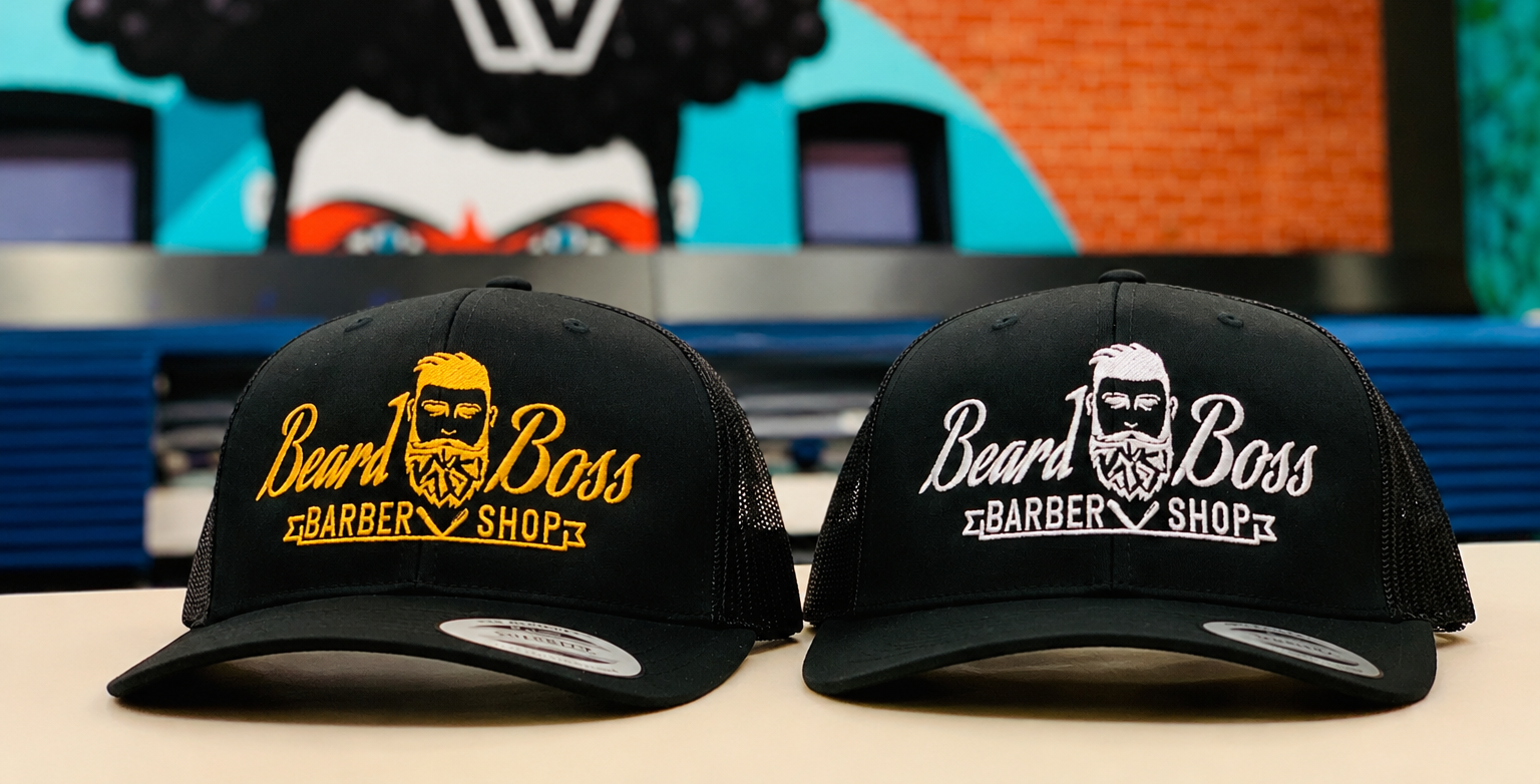Two Beard Boss Barbershop hats on a table at the Rockwall location