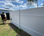 Contractor installing a white vinyl privacy fence alongside a residential lawn