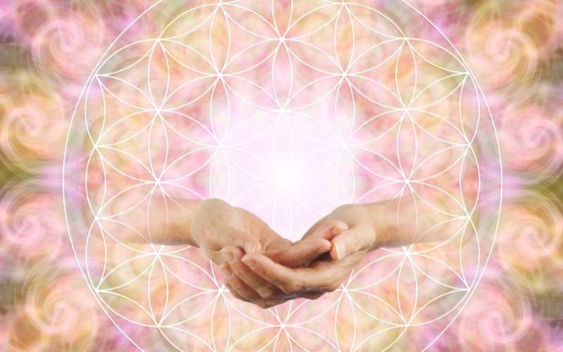 Flower of Life sacred geometry pattern glowing with open cupped hands held at the luminous centre