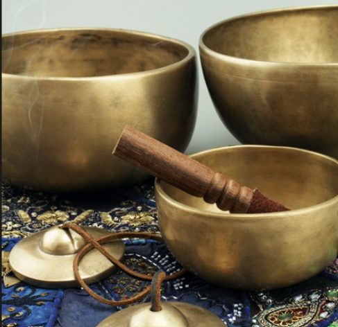 Tibetan singing bowls with wooden striker mallet and tingsha cymbals resting on ornate embroidered silk