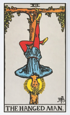 The Hanged Man tarot card (Rider-Waite-Smith) depicting a serene figure suspended upside-down by one ankle from a living wooden T-cross with leafy shoots, with a radiant golden halo around his head